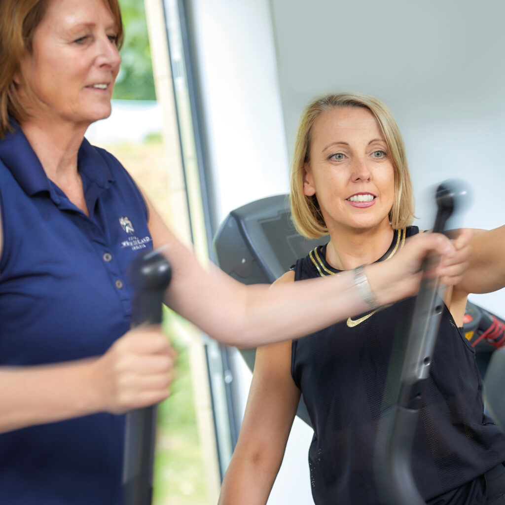 Tracey Pinfold guiding a client during a personal training session using a cardio machine.