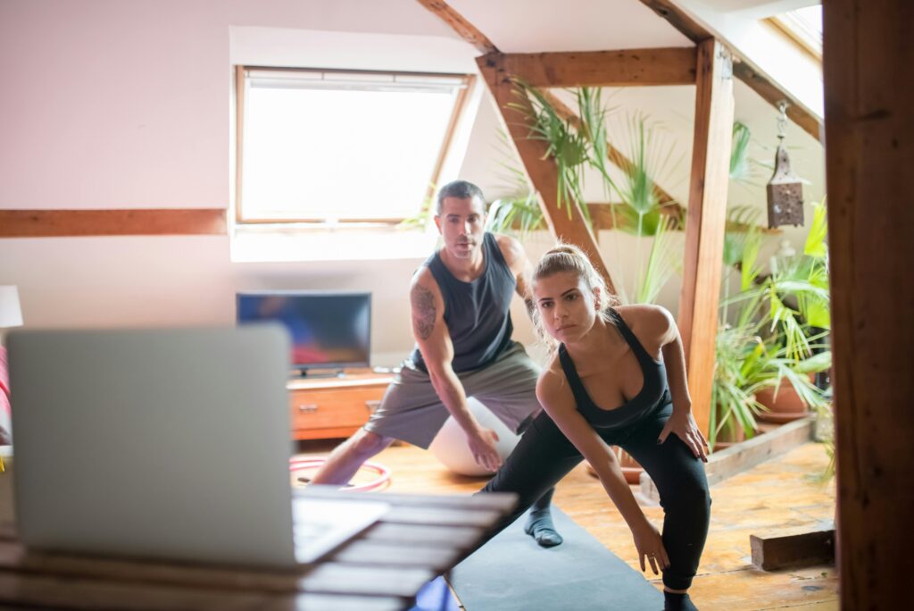 Couple exercising at home while following an online workout on a laptop.