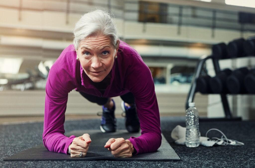 Woman with grey hair holding a plank on a gym mat.