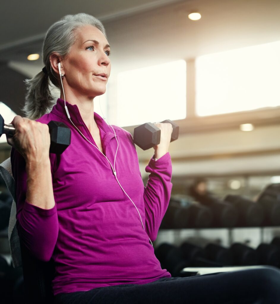 Woman with grey hair doing seated bicep curls with dumbbells in a gym.