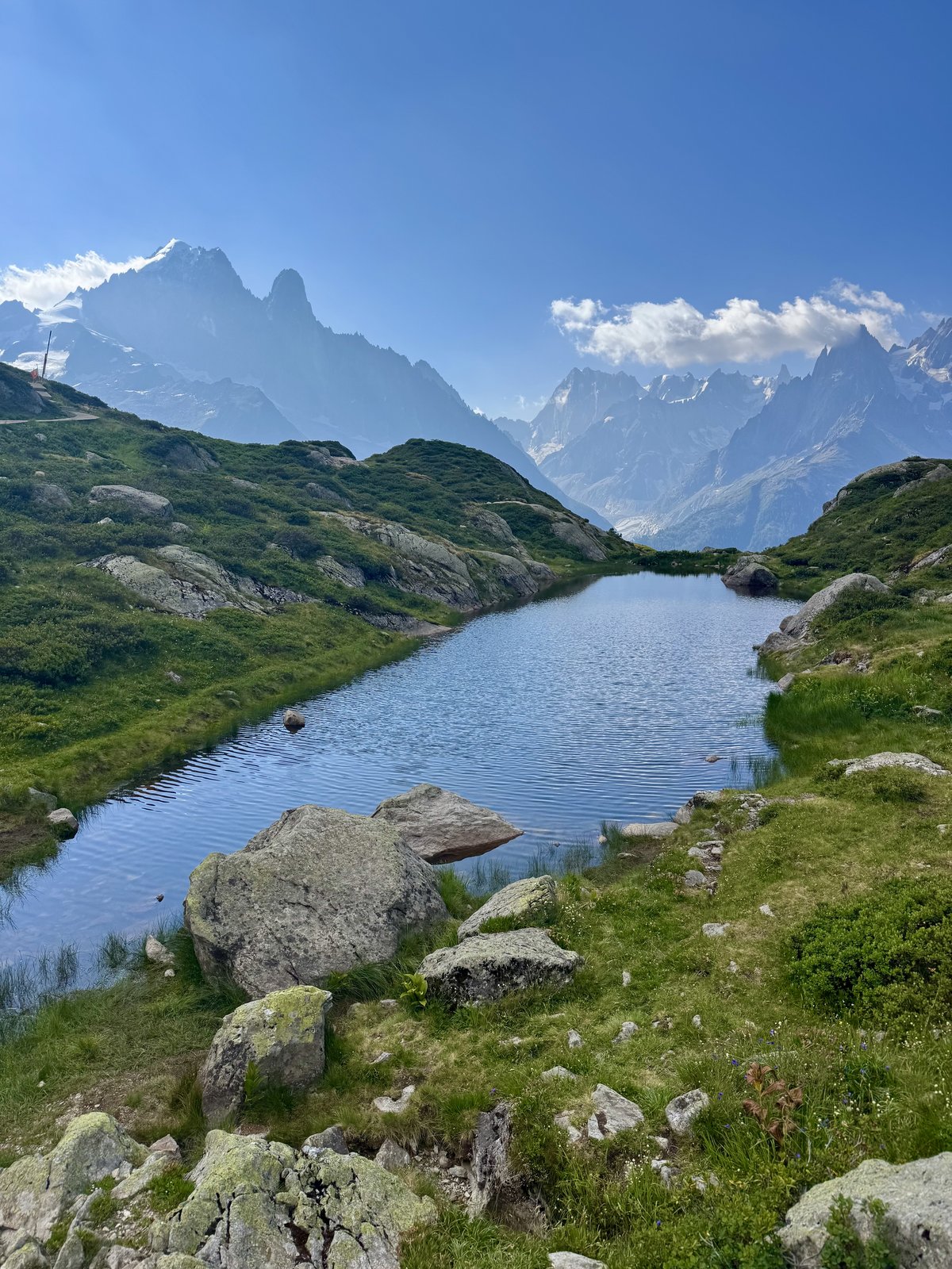 A still alpine tarn on the Tour du Mont Blanc mirroring the surrounding peaks under a clear blue sky