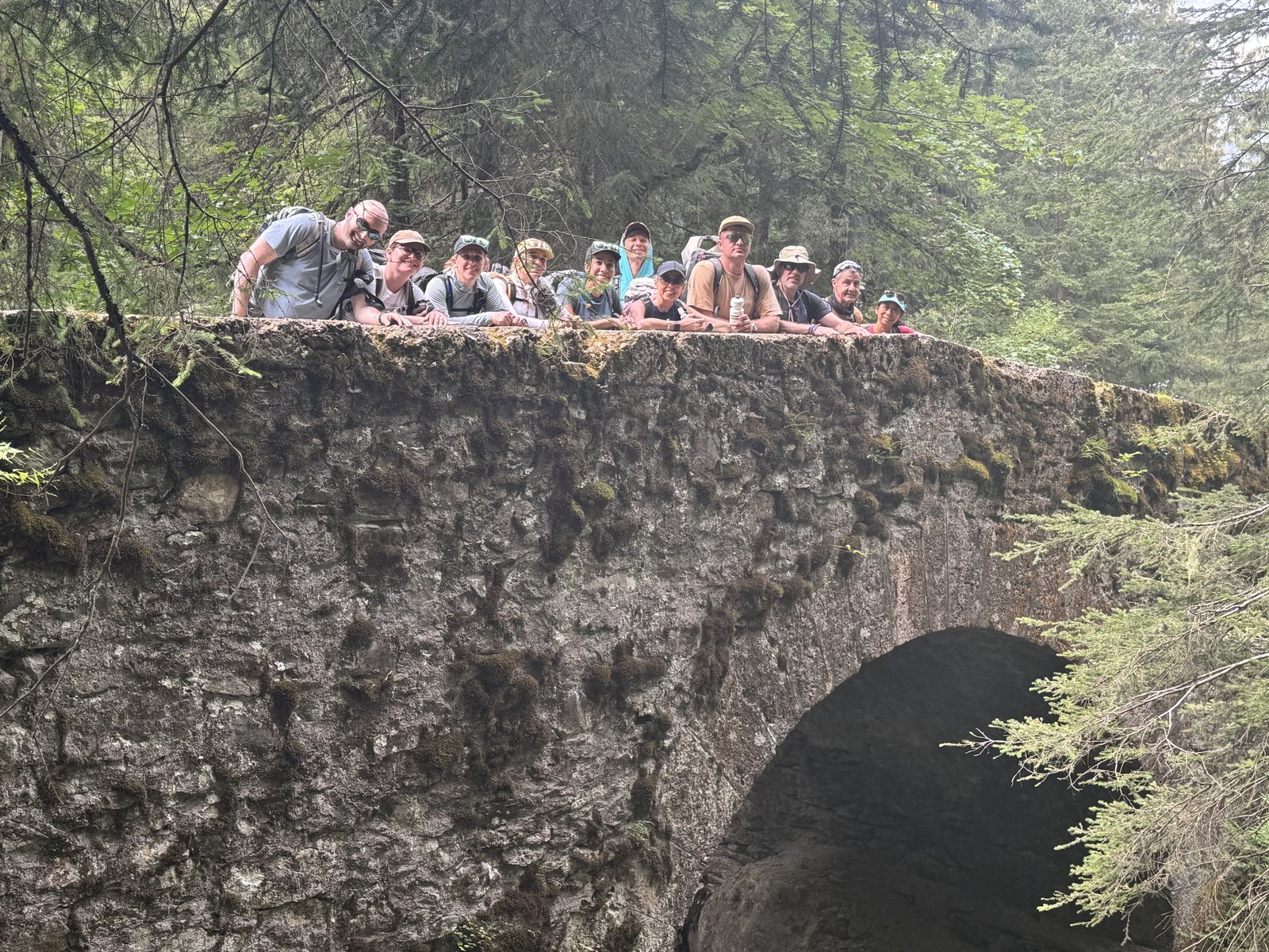 Walkers on the Tour du Mont Blanc leaning over the parapet of an old stone bridge in woodland